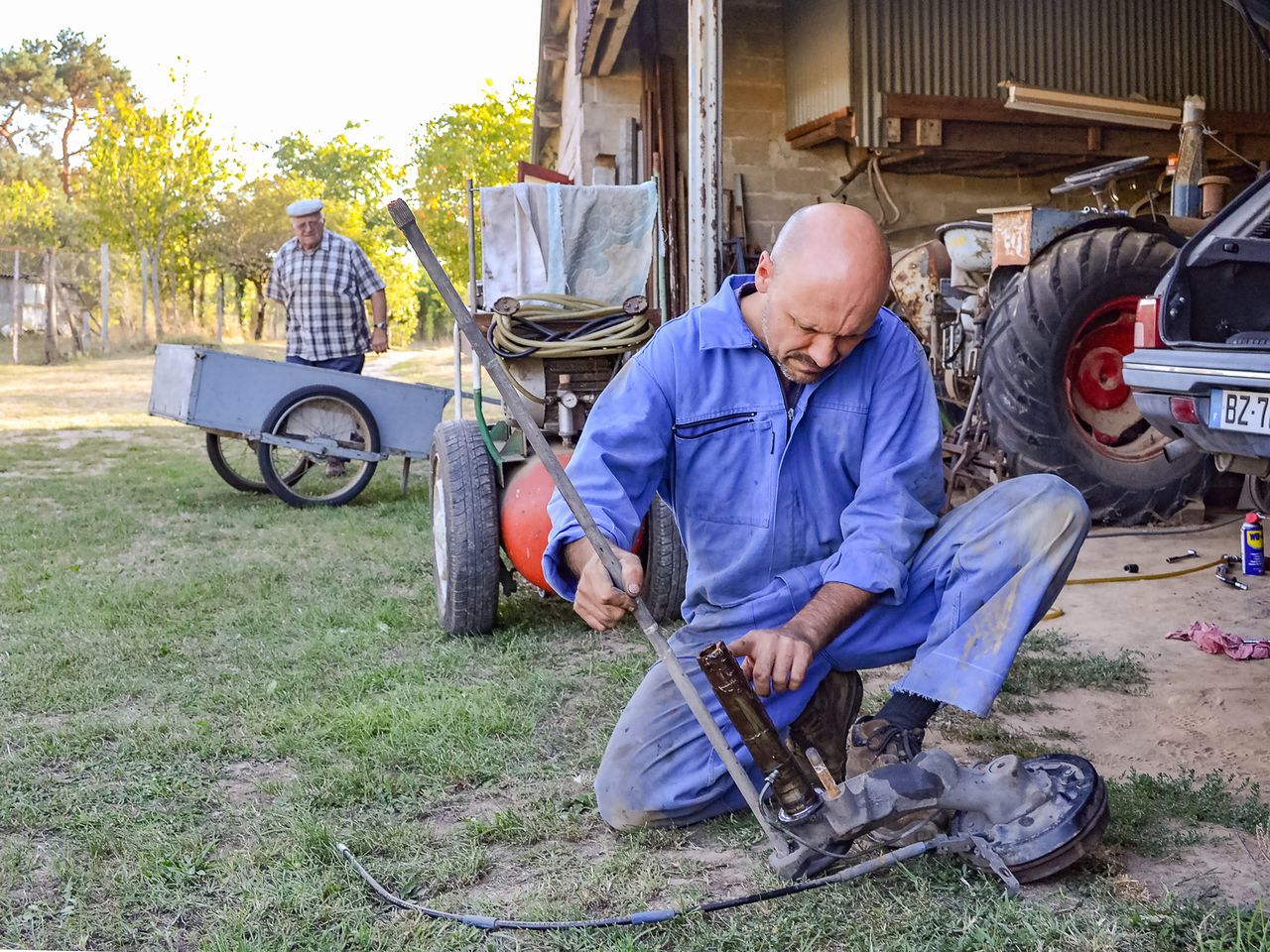 Two men working on farm equipment in rural France, showcasing hands-on mechanics and outdoor work.
