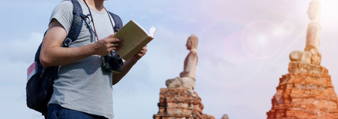 services-01 Man with a camera and book exploring ancient ruins under bright sun.