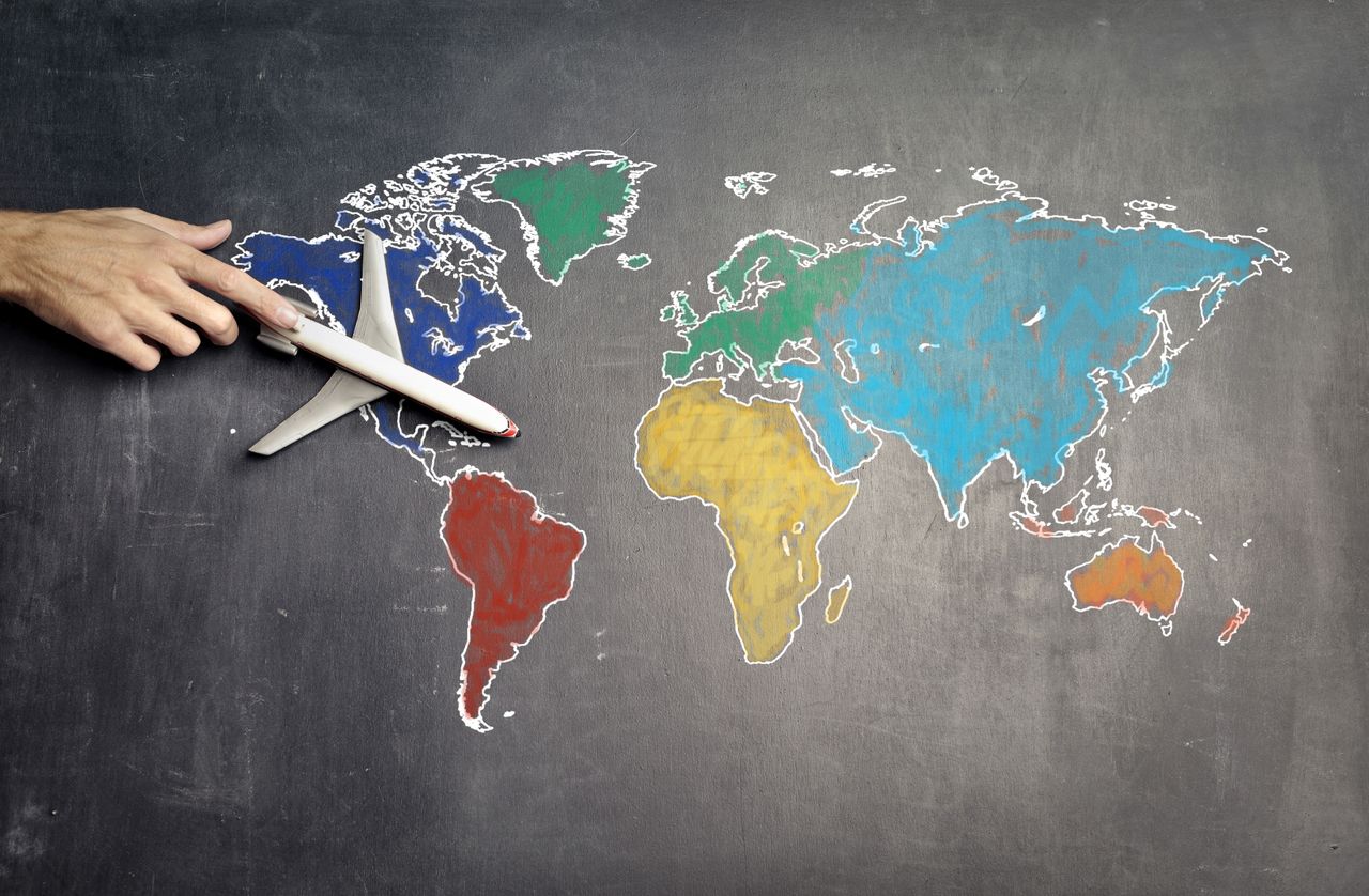 services-02 Top view of crop anonymous person holding toy airplane on colorful world map drawn on chalkboard